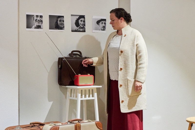 Beate Krist als Miep Gies im Bühnenbild. Sie bedient ein Radio. An der Wand hängen Schwarz-Weiss-Fotografien.