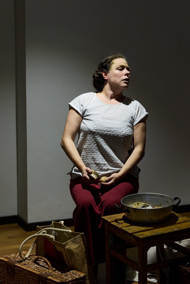 Szenenfoto. Beate Krist als Miep Gies sitzt auf einem Hocker und putzt Gemüse.
