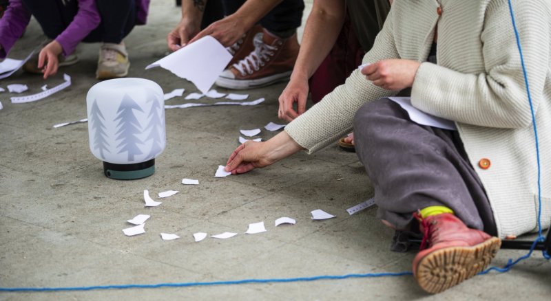 Publikum sitzt auf dem Boden und legt Papierschnipsel wie einen Weg aus