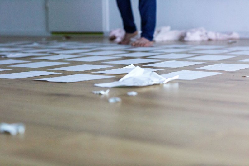 Auf dem Bühnenboden liegen Papierblätter ausgebreitet, zerknüllte Blätter ringsum