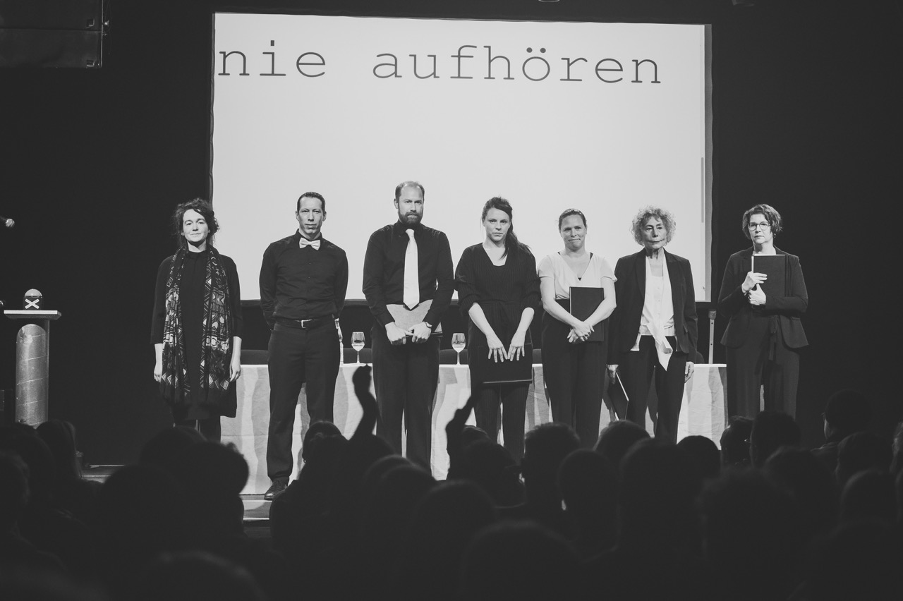 Ensemble beim Schlussapplaus, auf der Leinwand im Hintergrund steht: „nie aufhören“; Correctiv-Lesung